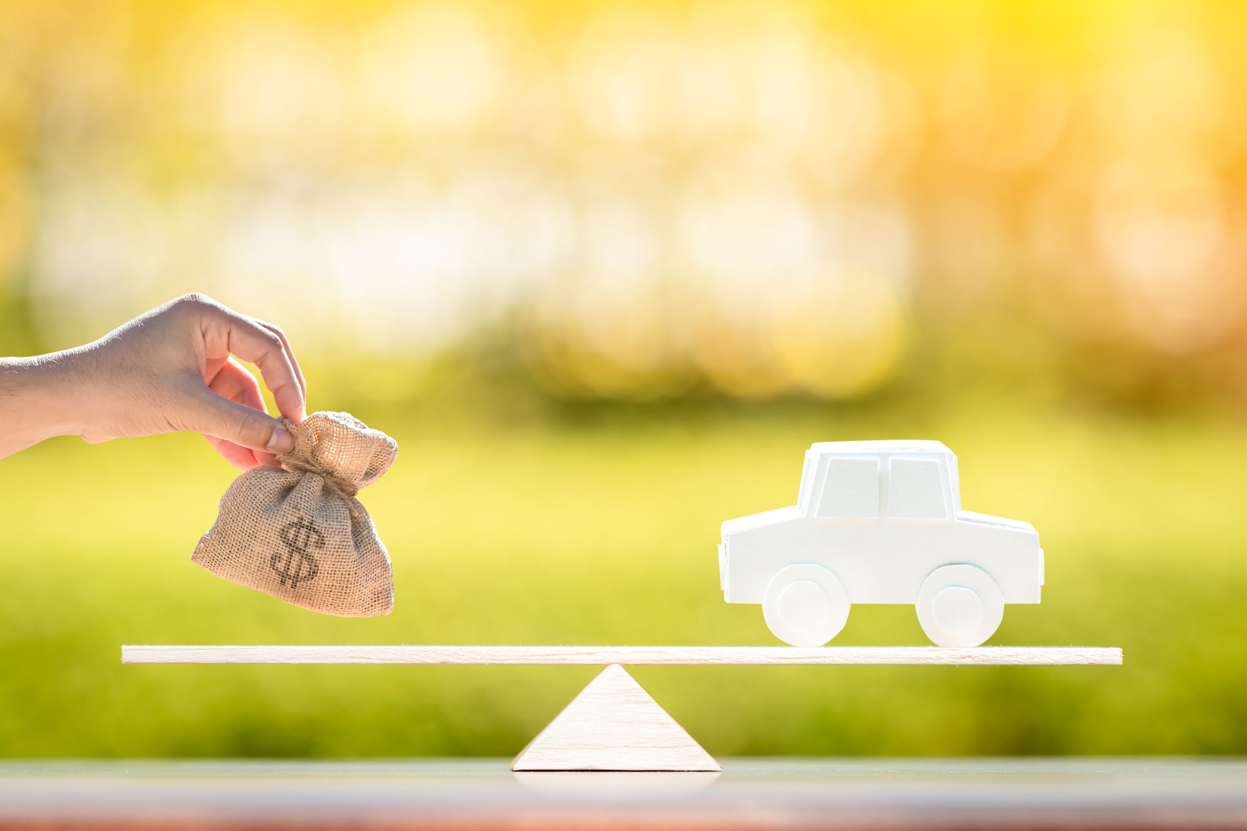 Woman hand hold a money bag put on the scales with balance versus the car model she is looking to trade in